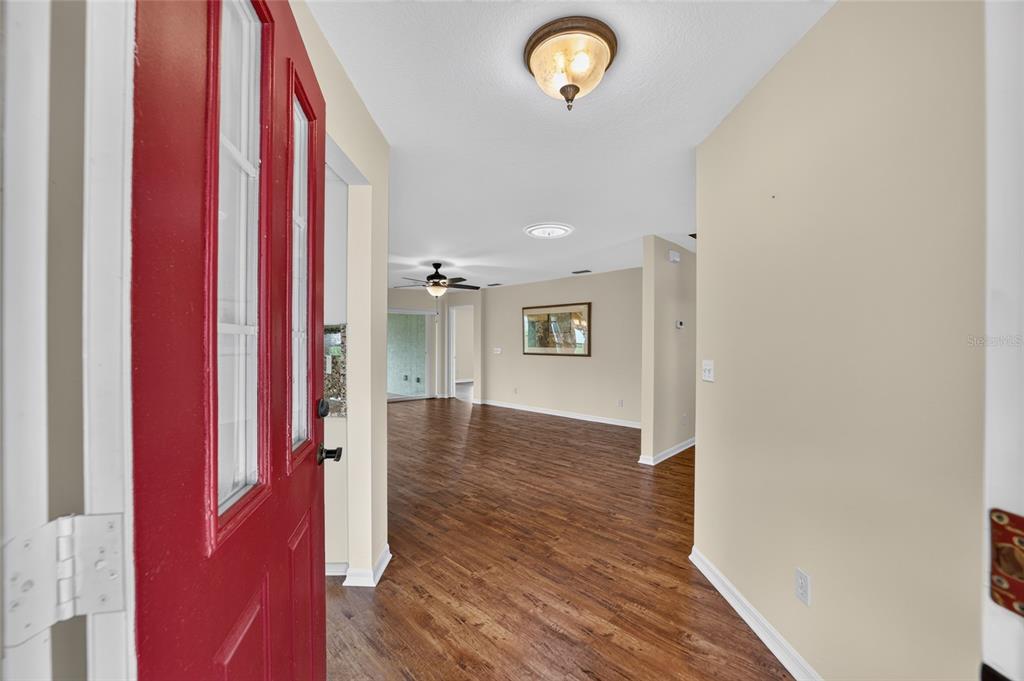 An entryway with a red door opens into a living area with wood-look flooring — 9702 SW 92ND PLACE ROAD, OCALA, FL