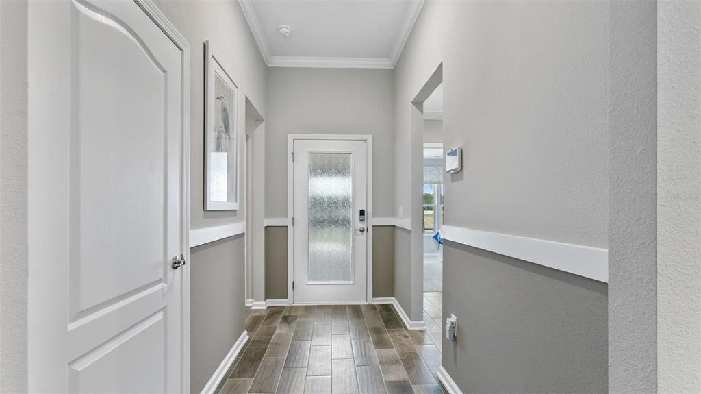 A bright entryway features gray walls with white wainscoting, wood-look tile flooring, and a glass-paneled door — 142 GREENWOOD DRIVE, PALM COAST, FL