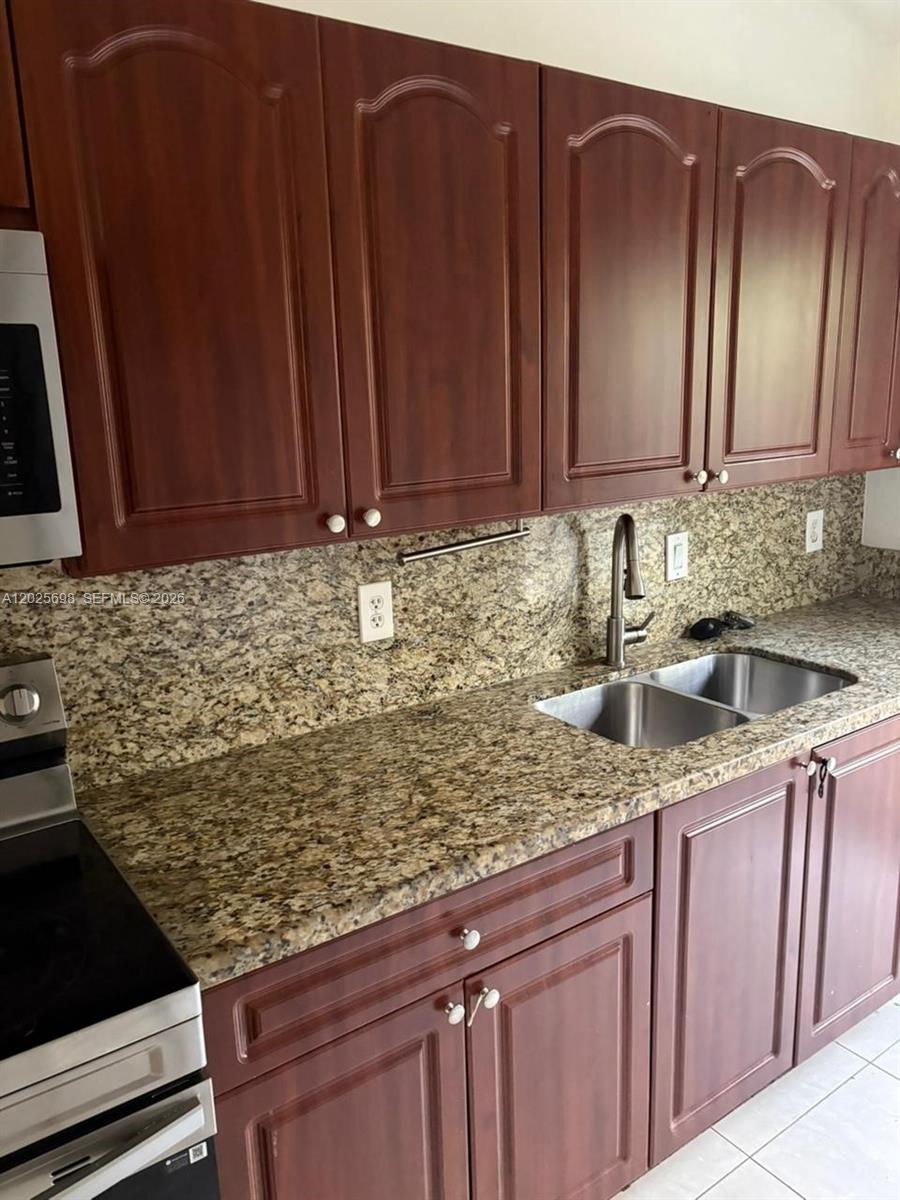 A kitchen features dark wood cabinets, granite countertops, and a stainless steel double sink — 117 SE 3rd Ave # 7, Hallandale Beach FL 33009, HALLANDALE BEACH, FL
