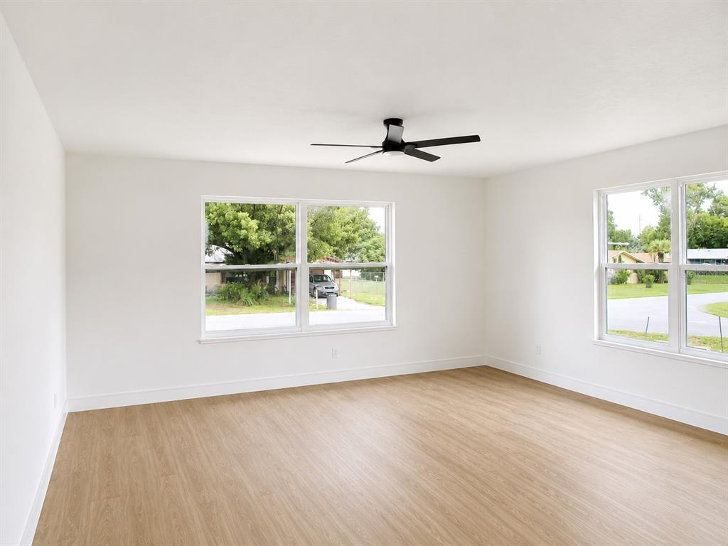 An empty room features light wood-look flooring, white walls, a black ceiling fan, and windows — 49 LAKE COURT LOOP, OCALA, FL