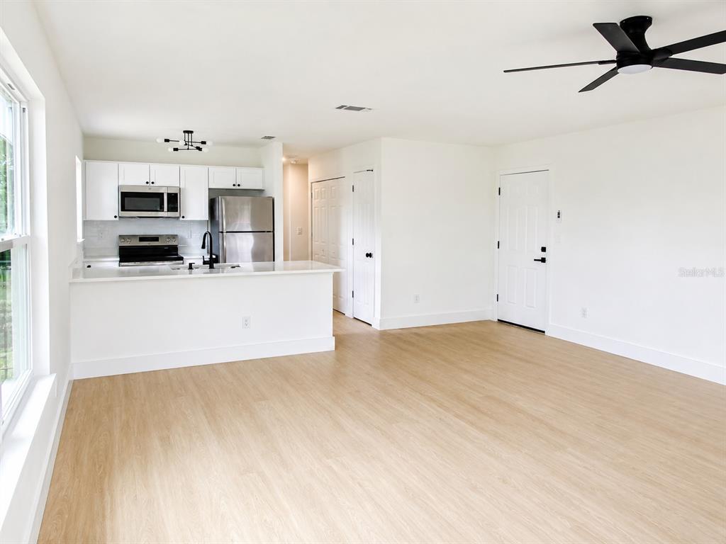 An open-concept kitchen and living area with light wood flooring and white cabinetry — 49 LAKE COURT LOOP, OCALA, FL