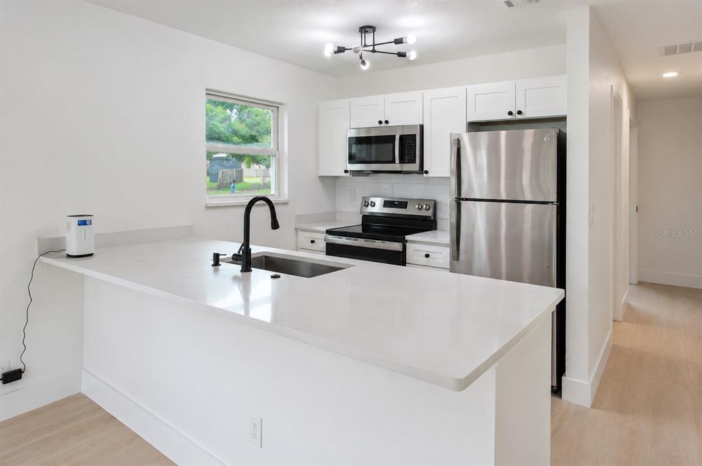 A kitchen features white cabinets, stainless steel appliances, a quartz island, and a black faucet — 49 LAKE COURT LOOP, OCALA, FL