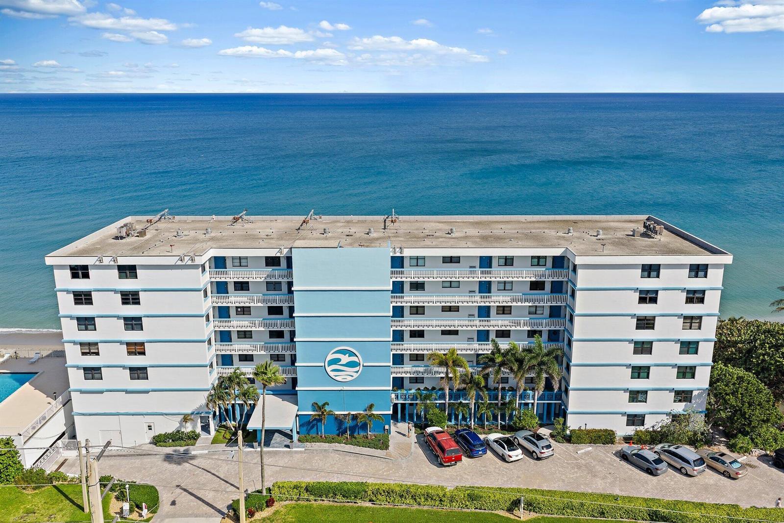 An aerial view shows a multi-story oceanfront apartment building with a parking lot and beach — 900 Ocean Drive # 106, Juno Beach FL 33408, JUNO BEACH, FL