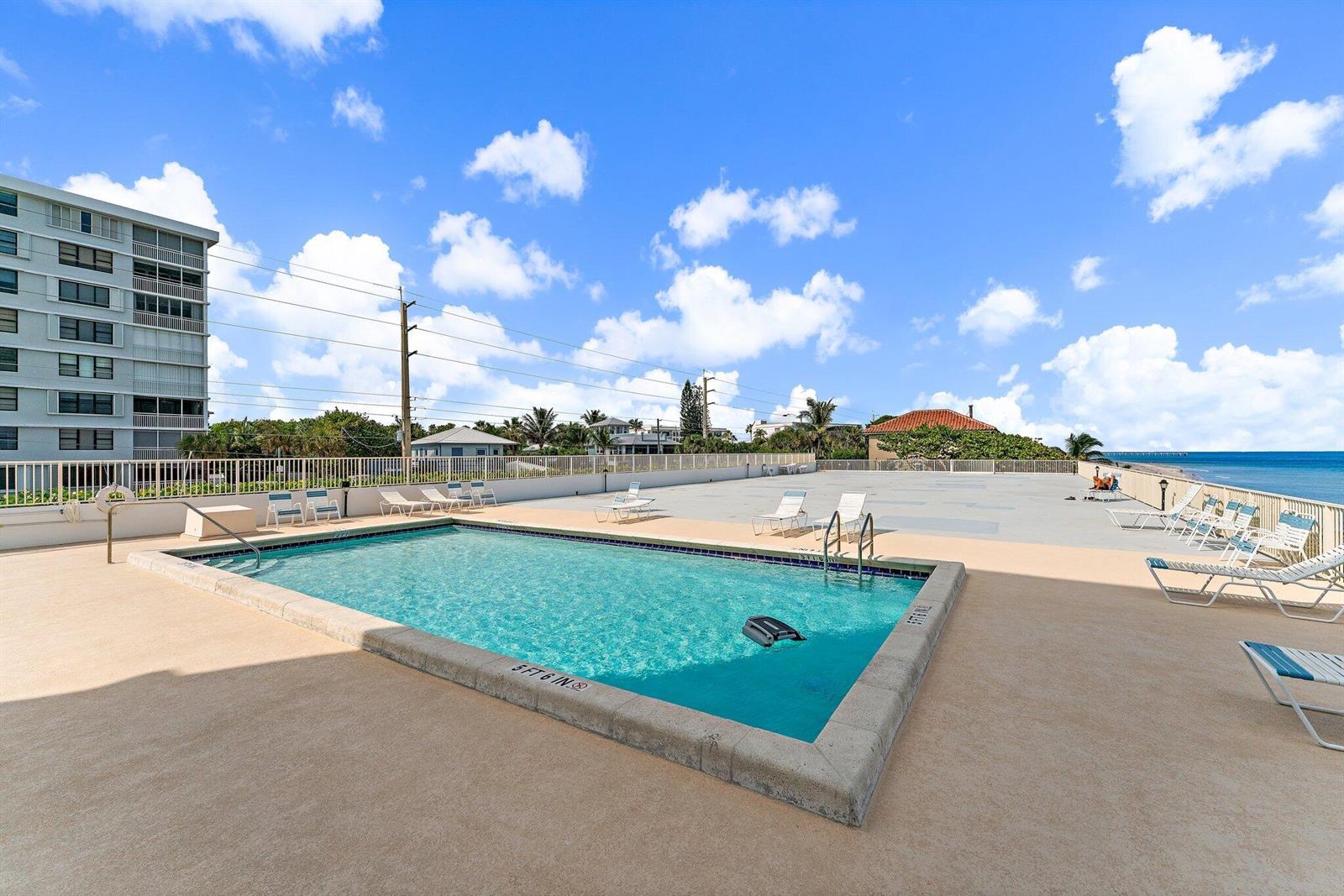 An outdoor swimming pool with lounge chairs on a deck overlooking the ocean — 900 Ocean Drive # 106, Juno Beach FL 33408, JUNO BEACH, FL