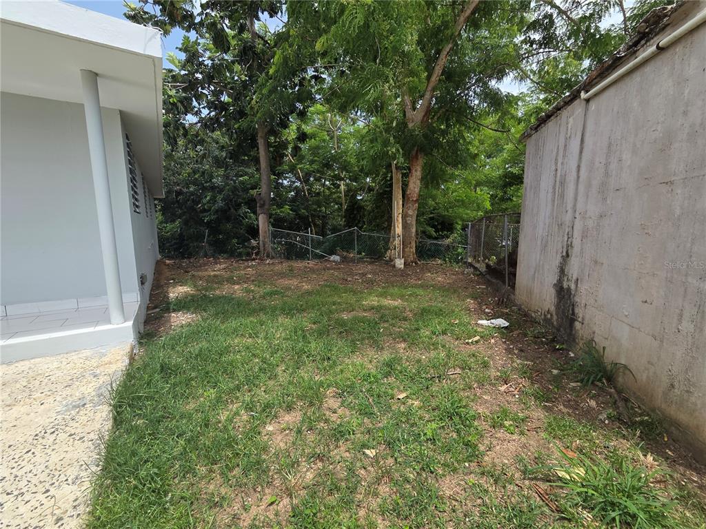 A grassy side yard sits between a white house and a concrete wall — Colinas de Vista Alegre COLINAS DE VISTA ALEGRE, BAYAMON, PR