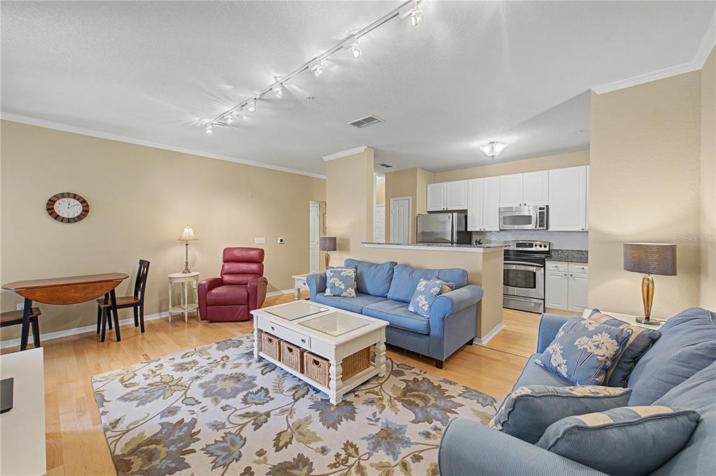 An open-concept living room and kitchen featuring hardwood floors, blue sofas, and track lighting — 4221 W SPRUCE STREET UNIT 1222, TAMPA, FL