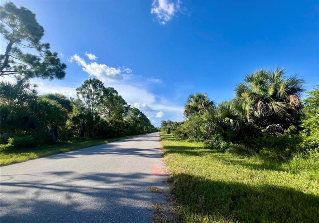 A paved road stretches through a sunny, undeveloped area with lush green trees and vegetation — 2071 LINGAYEN STREET, PORT CHARLOTTE, FL