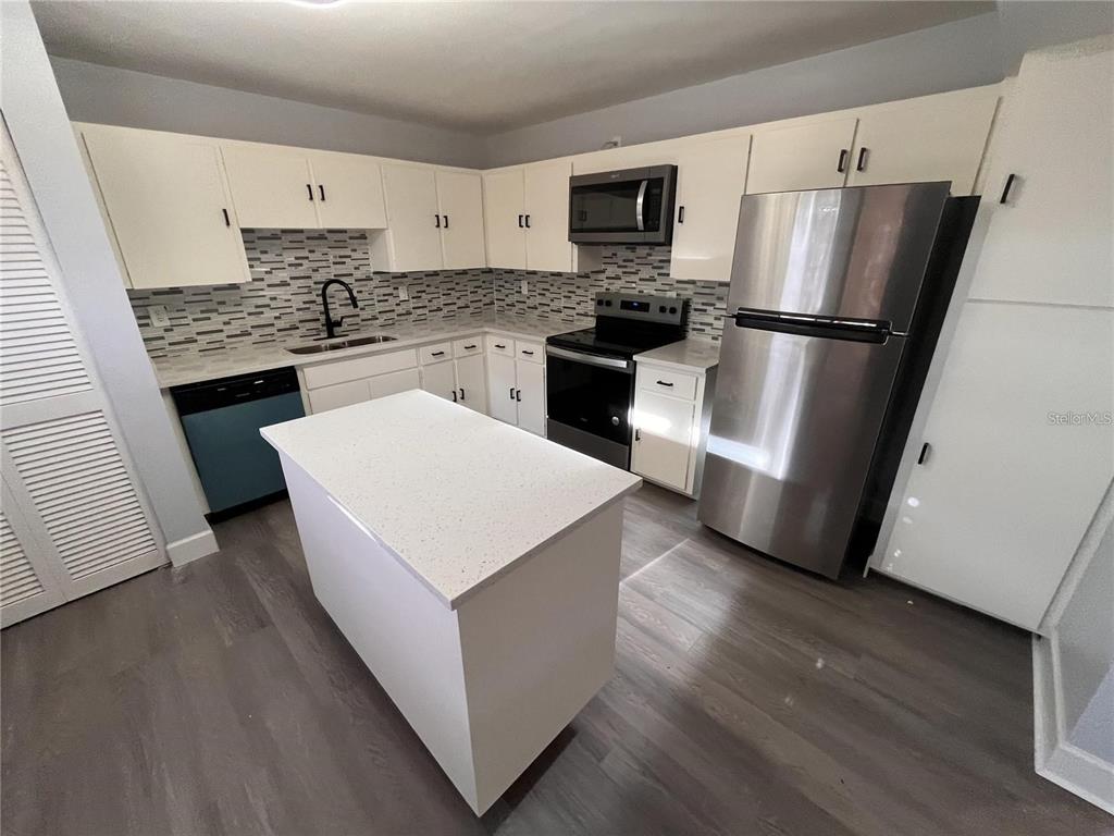 A kitchen features white cabinets, stainless steel appliances, a center island, and a tiled backsplash — 314 SPRING LAKES BOULEVARD UNIT 314-U, BRADENTON, FL