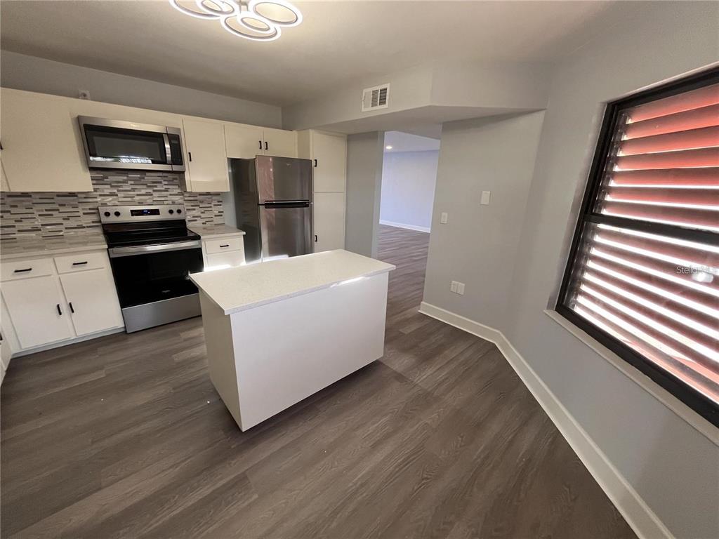 A kitchen features white cabinets, stainless steel appliances, a center island, and wood-look flooring — 314 SPRING LAKES BOULEVARD UNIT 314-U, BRADENTON, FL