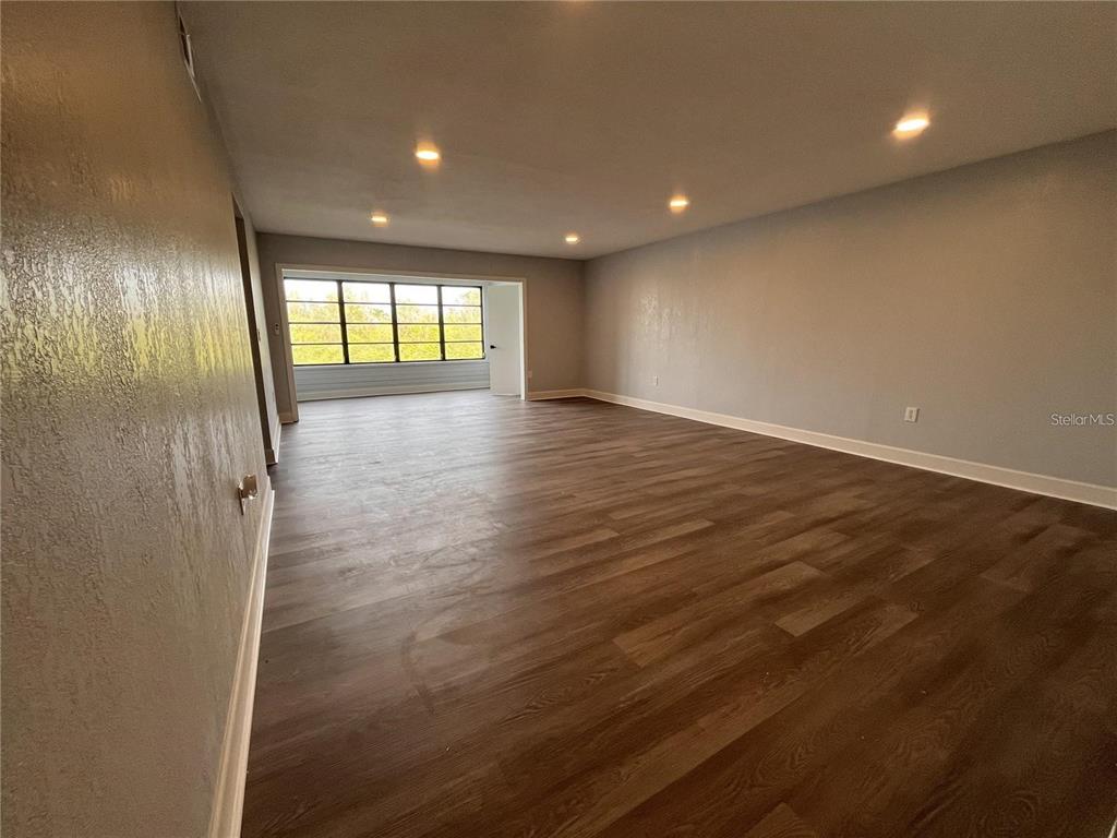 An empty room features wood-look flooring, recessed lighting, and a large window overlooking the outdoors — 314 SPRING LAKES BOULEVARD UNIT 314-U, BRADENTON, FL
