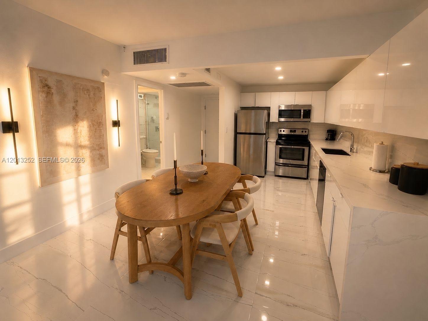 A modern kitchen and dining area features white marble floors, stainless steel appliances, and wood furniture — 2301 Collins Ave # 628, Miami Beach FL 33139, MIAMI BEACH, FL