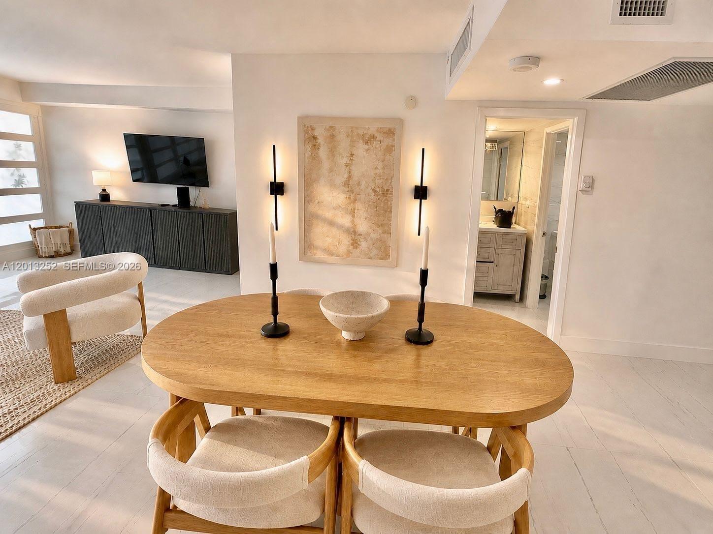 A dining area features an oval wooden table, modern wall sconces, and light-colored flooring — 2301 Collins Ave # 628, Miami Beach FL 33139, MIAMI BEACH, FL