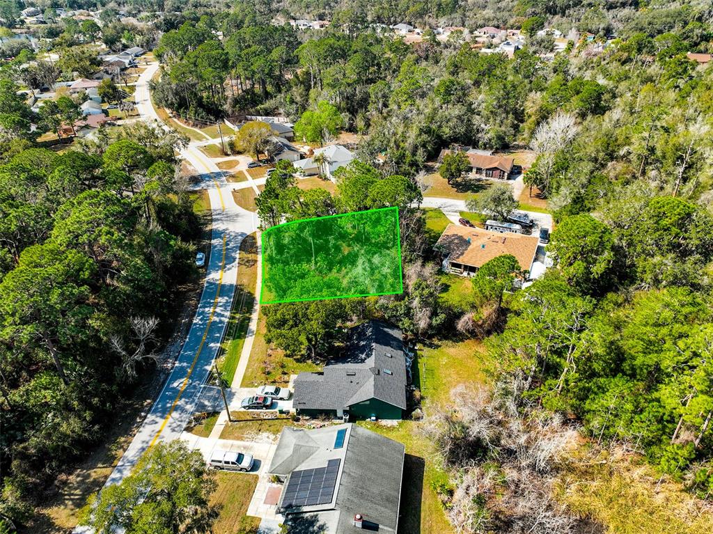 An aerial view shows a vacant, wooded lot highlighted in green next to residential houses — 632 ANDERSON DRIVE, DELTONA, FL