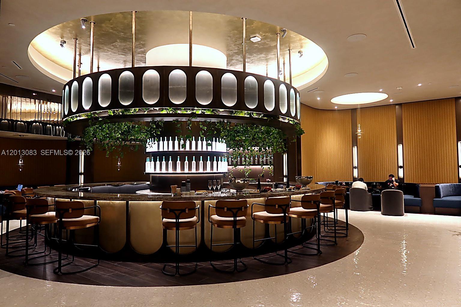 A circular bar with modern stools sits beneath a large, illuminated, gold-accented ceiling fixture — 20 NE 11 st # 3403B, Miami FL 33132, MIAMI, FL