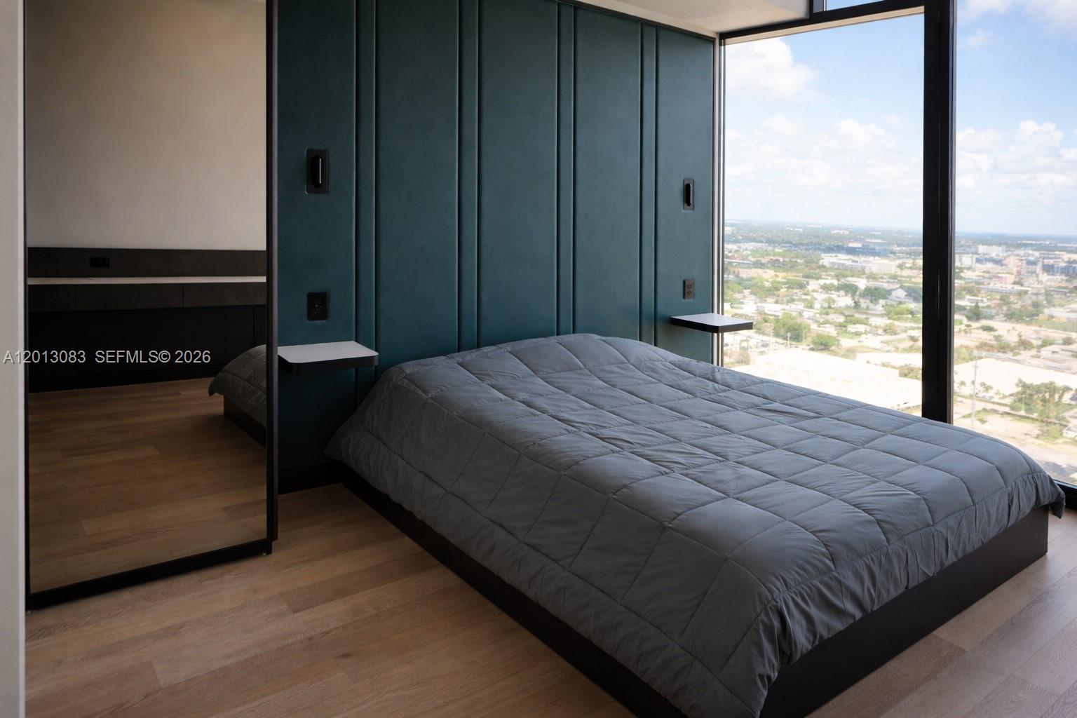 A bedroom features a dark green paneled headboard, a grey quilt, and floor-to-ceiling windows — 20 NE 11 st # 3403B, Miami FL 33132, MIAMI, FL
