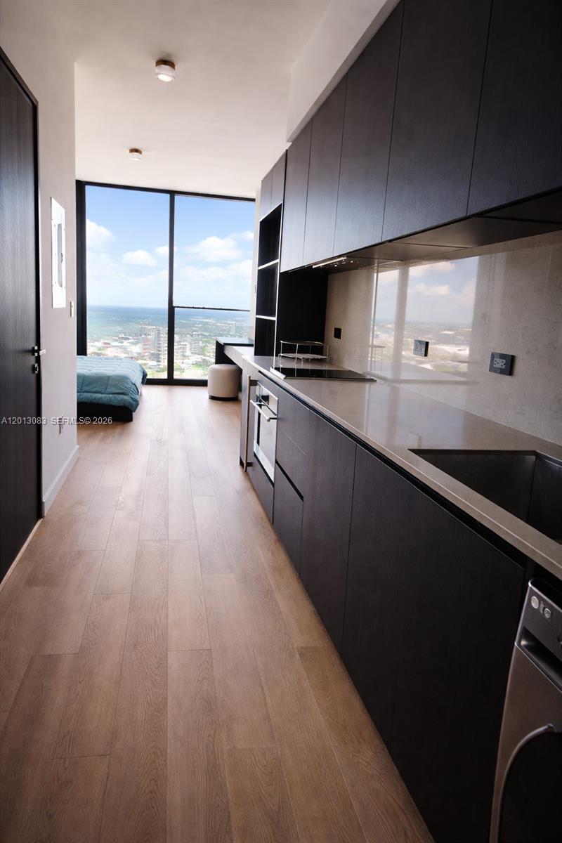 A modern kitchen with dark cabinetry and light countertops overlooks a bedroom with floor-to-ceiling windows — 20 NE 11 st # 3403B, Miami FL 33132, MIAMI, FL