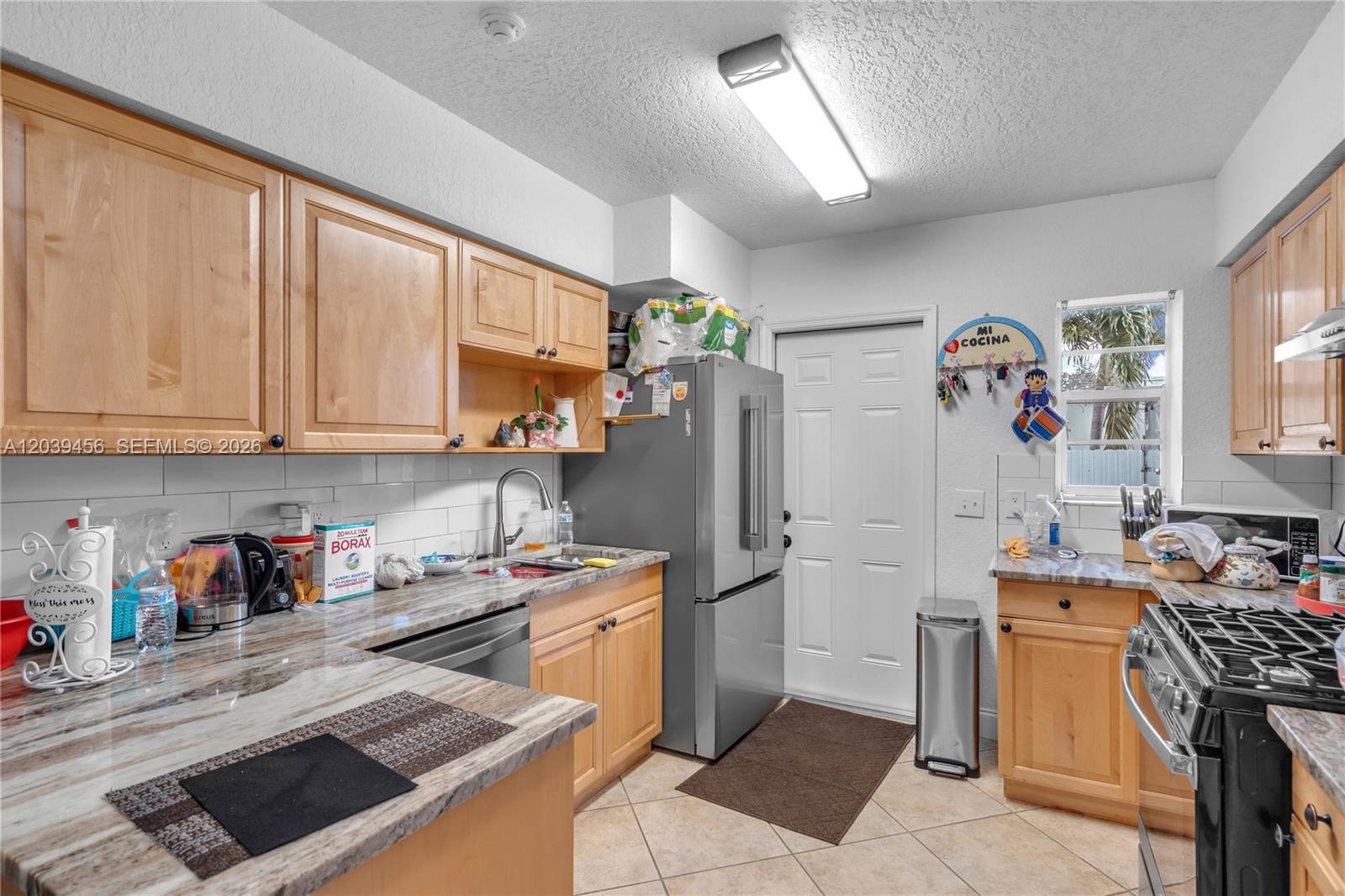 A kitchen features light wood cabinets, granite countertops, stainless steel appliances, and a white door — FORT LAUDERDALE, FL