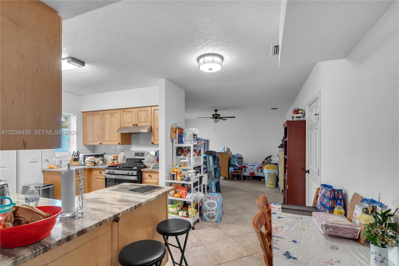 A kitchen with light wood cabinets and granite countertops opens into a living area — FORT LAUDERDALE, FL
