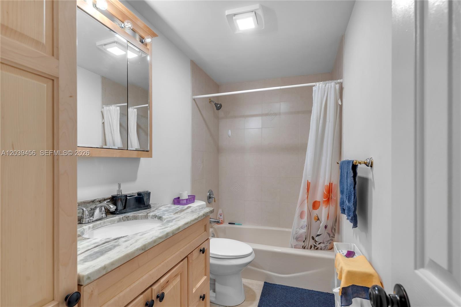A bathroom features a light wood vanity with a stone countertop, toilet, and shower-tub combo — FORT LAUDERDALE, FL