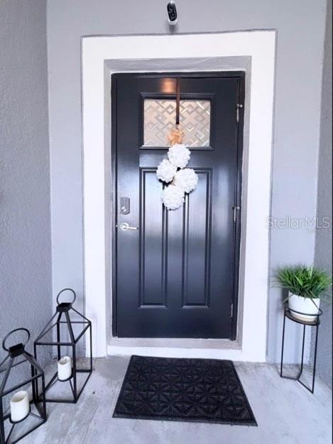 A black front door with a decorative wreath sits on a porch with lanterns and plants — 6047 ACARA LANE, LAND O LAKES, FL