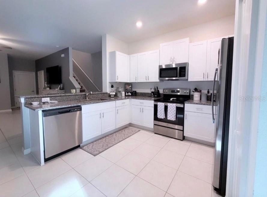 A kitchen with white cabinets, stainless steel appliances, granite countertops, and light-colored tile flooring — 6047 ACARA LANE, LAND O LAKES, FL