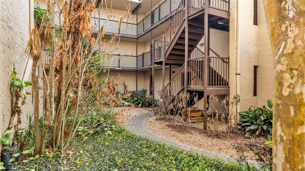 An outdoor courtyard features a paved walkway, landscaping, and a metal staircase leading to balconies — 2025 SYLVESTER ROAD UNIT N101, LAKELAND, FL