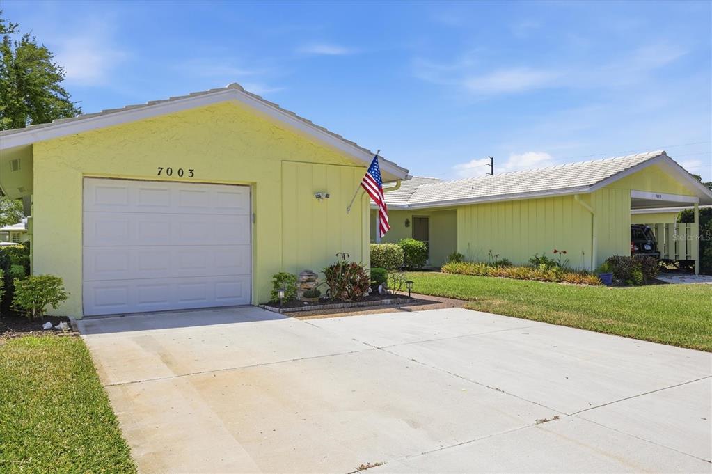 A yellow single-story house features a white garage door, a concrete driveway, and an American flag — 7003 10TH AVENUE W, BRADENTON, FL