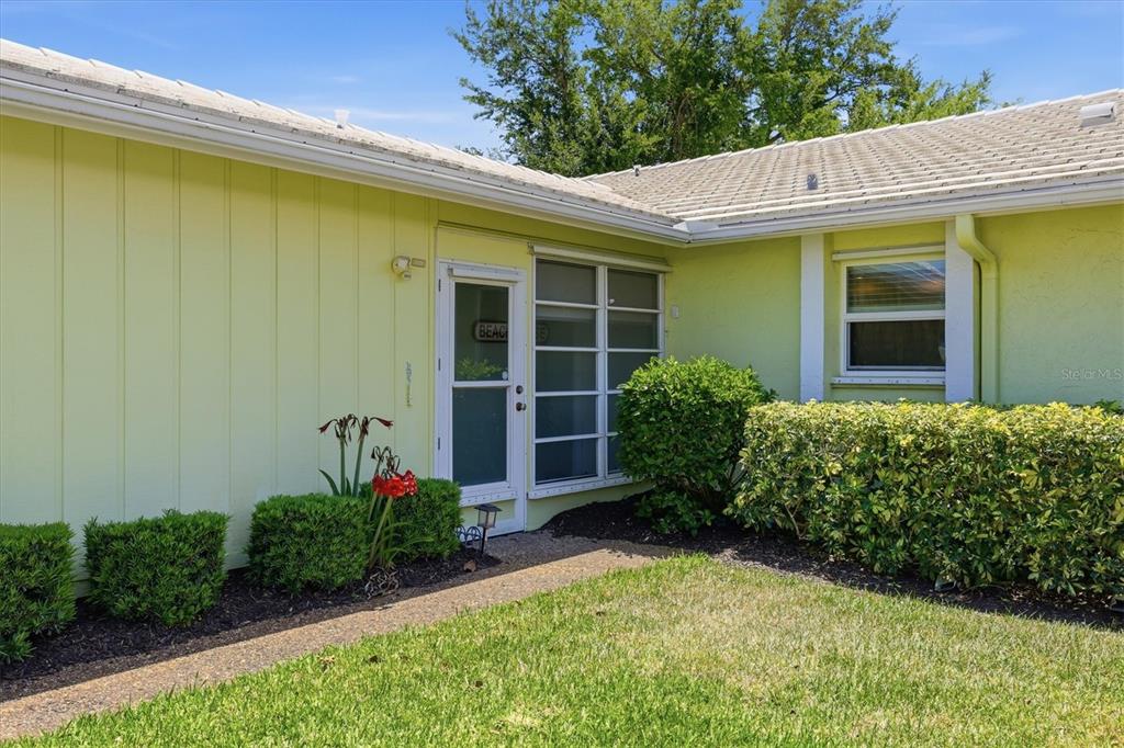 The exterior of a light green house features a white door and a small garden — 7003 10TH AVENUE W, BRADENTON, FL