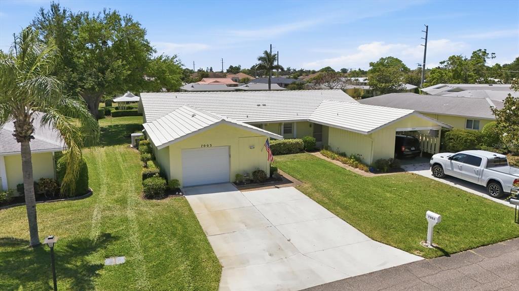 An exterior view of a yellow single-story house with a white roof and driveway — 7003 10TH AVENUE W, BRADENTON, FL