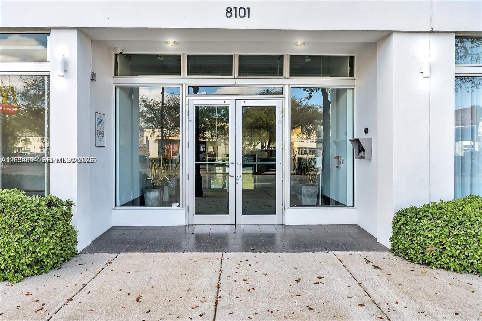 The exterior entrance of a commercial building features glass double doors and two large windows — 8101 Biscayne Blvd # 506, Miami FL 33138, MIAMI, FL