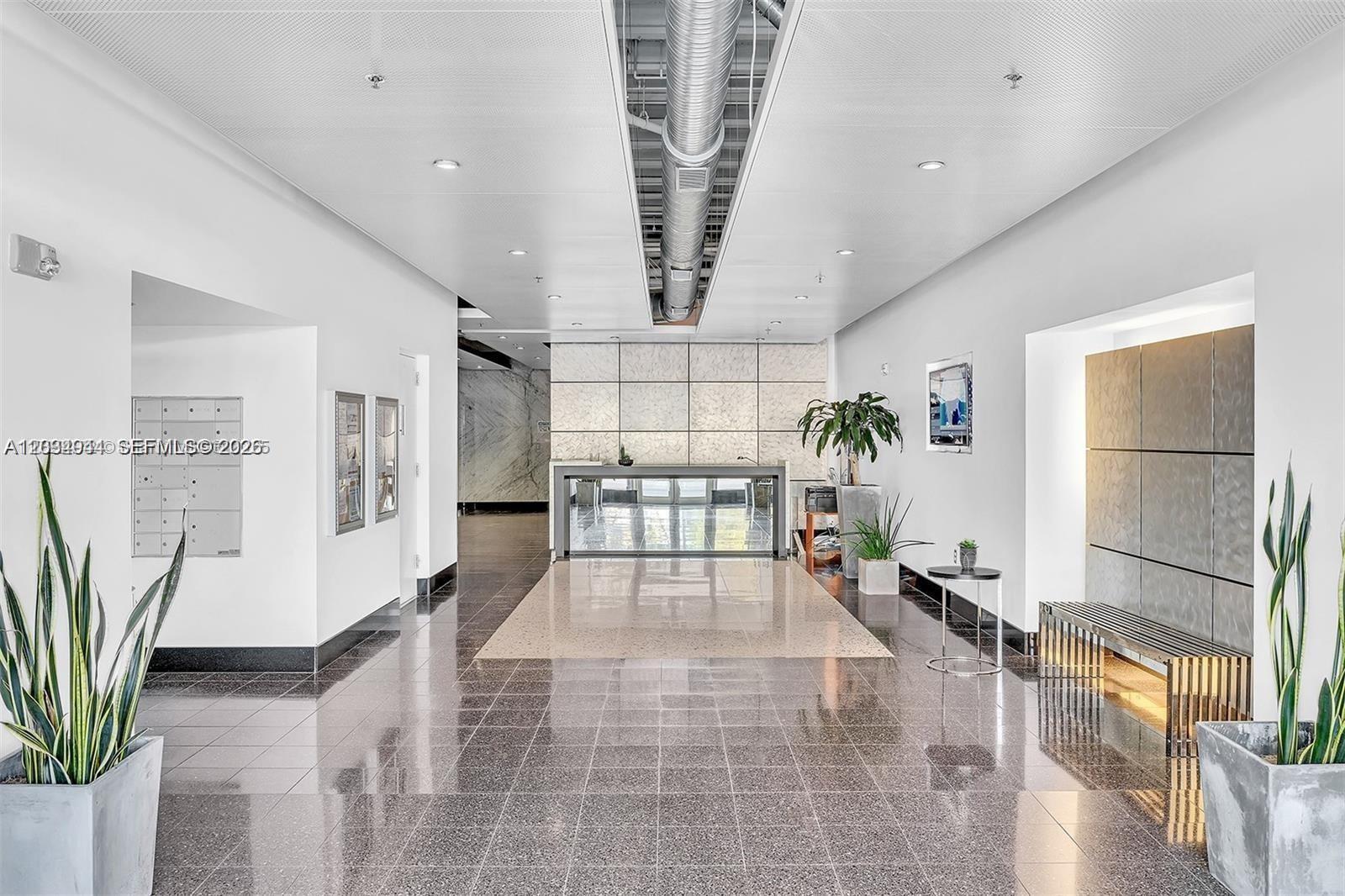 A modern lobby features a reception desk, tiled floors, recessed lighting, and decorative potted plants — 8101 Biscayne Blvd # 506, Miami FL 33138, MIAMI, FL