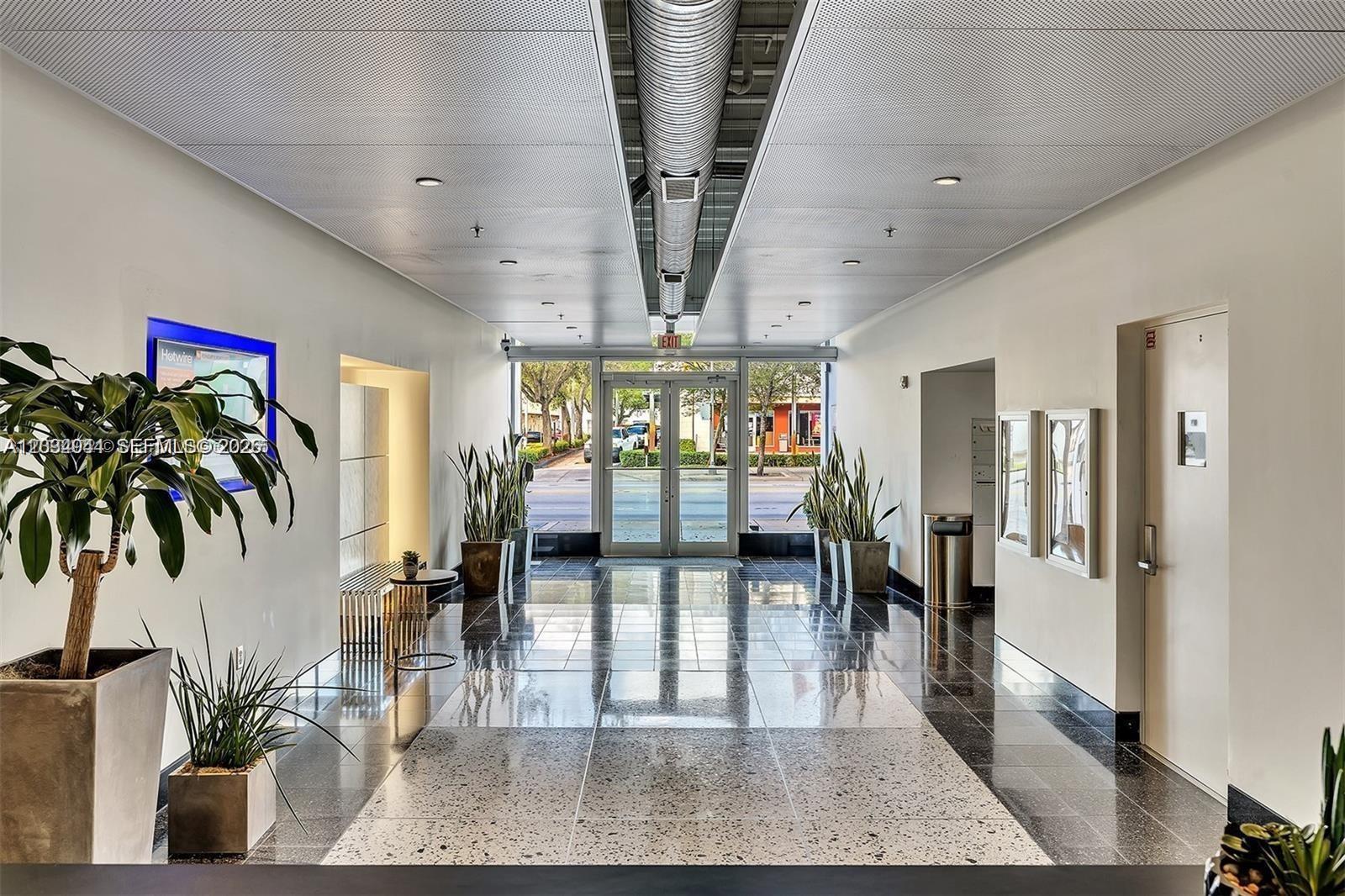 A modern building lobby features a polished tile floor, metallic ceiling, and glass entrance doors — 8101 Biscayne Blvd # 506, Miami FL 33138, MIAMI, FL