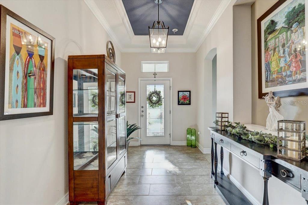 A bright entryway features a tray ceiling with blue paint, tile flooring, and decorative furniture — 7209 MEETING HOUSE LANE, APOLLO BEACH, FL