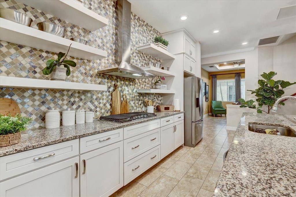 A kitchen features white cabinets, granite countertops, a mosaic tile backsplash, and floating shelves — 7209 MEETING HOUSE LANE, APOLLO BEACH, FL