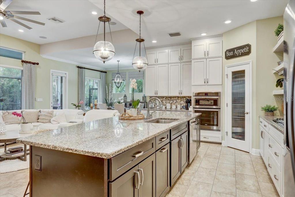 A kitchen features a granite-topped island, dark lower cabinets, white upper cabinets, and stainless appliances — 7209 MEETING HOUSE LANE, APOLLO BEACH, FL