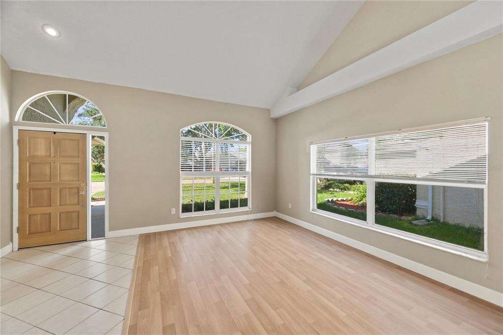 An empty living room features light wood flooring, vaulted ceilings, and large arched windows — 11213 CLAYRIDGE DRIVE, TAMPA, FL