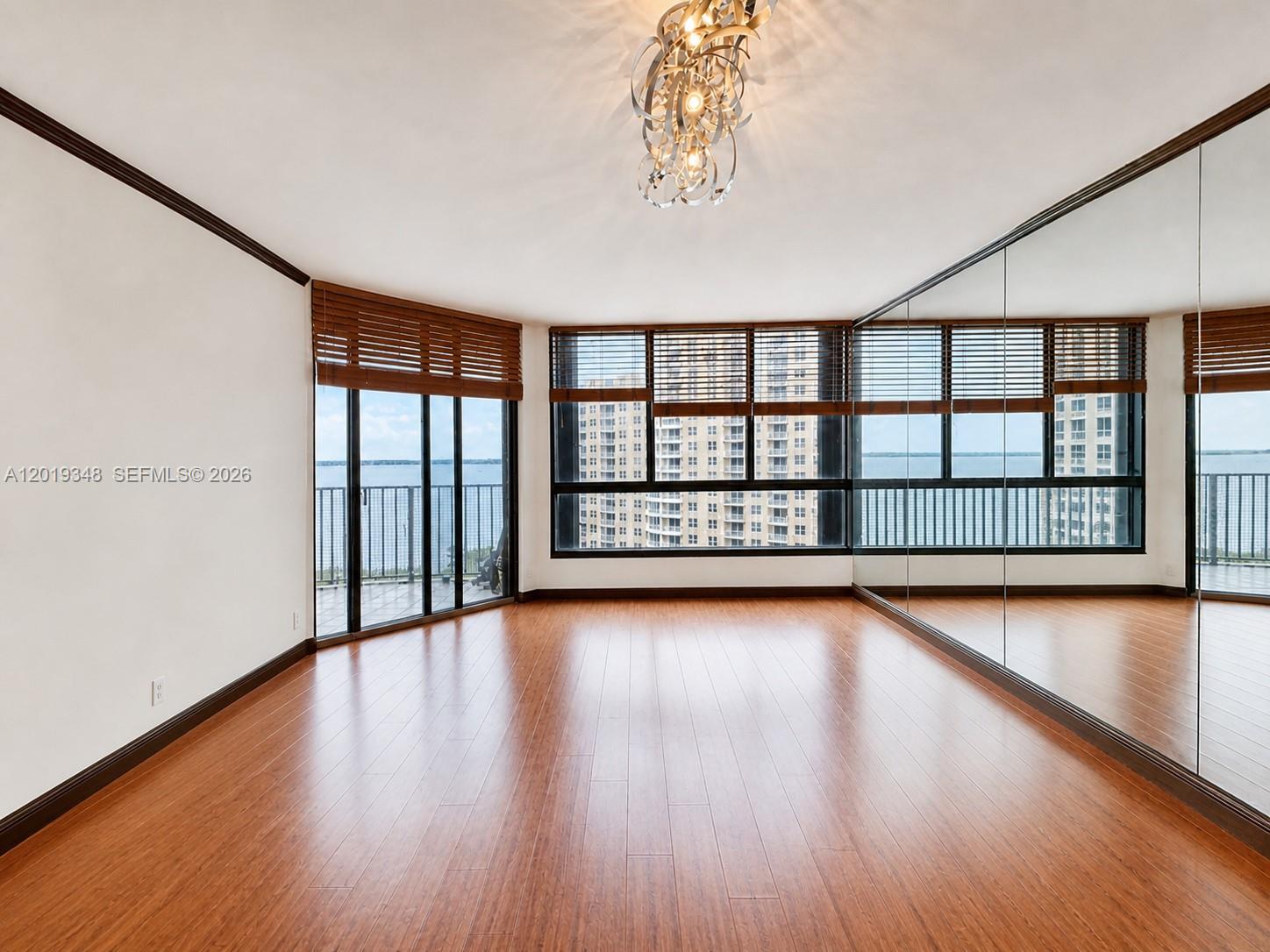 An empty room features hardwood floors, a mirrored wall, and large windows overlooking water — 520 Brickell Key Dr # A1113, Miami FL 33131, MIAMI, FL