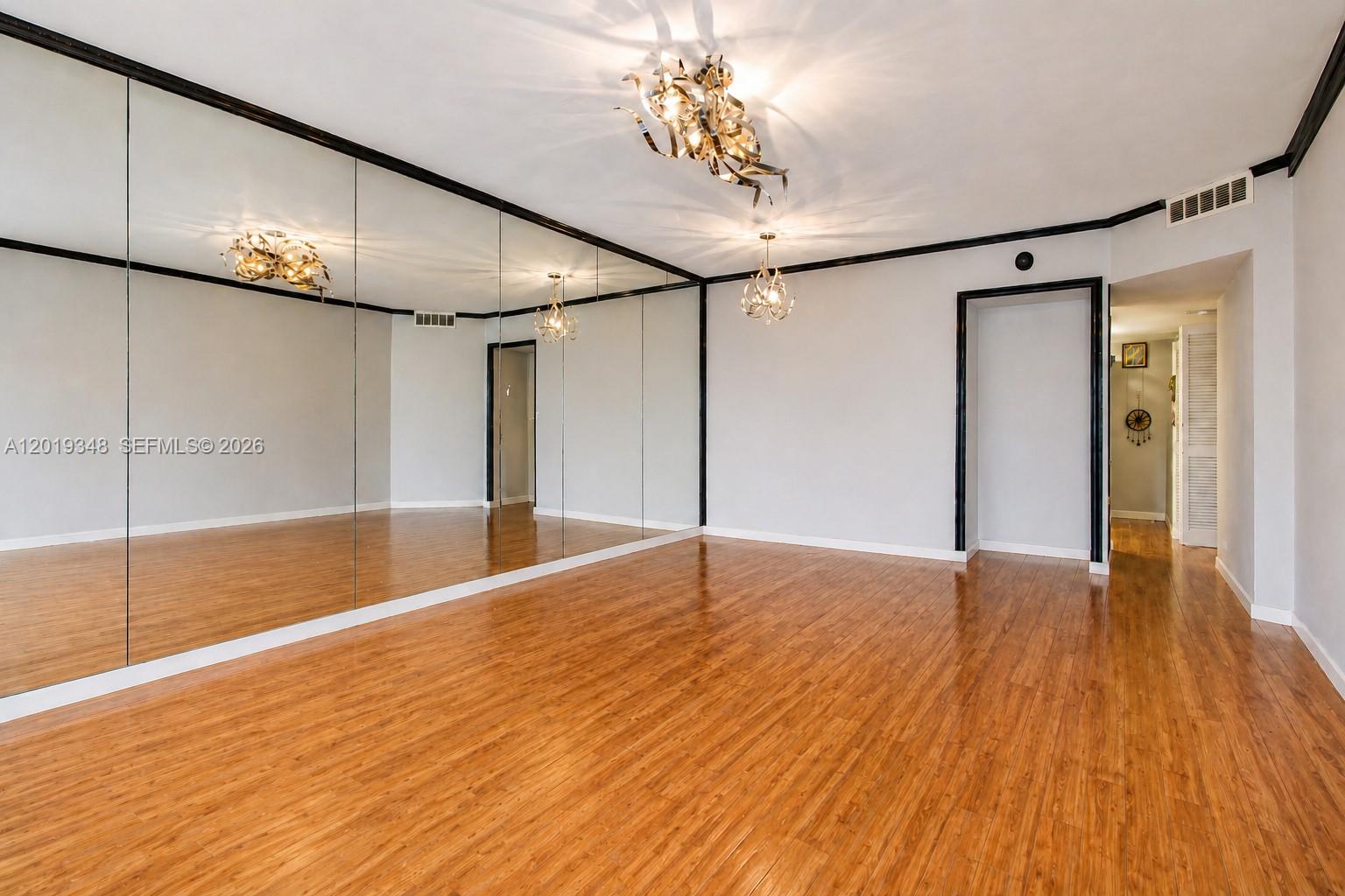 A room with wood flooring, mirrored walls, and two decorative light fixtures — 520 Brickell Key Dr # A1113, Miami FL 33131, MIAMI, FL