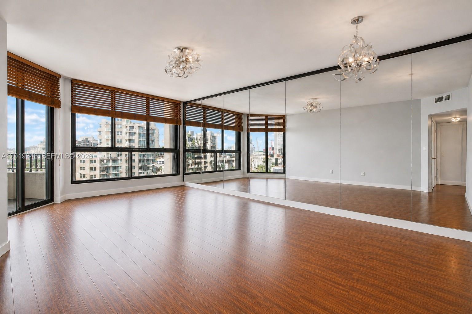 An empty room features wood-look flooring, a mirrored wall, and large windows with wooden blinds — 520 Brickell Key Dr # A1113, Miami FL 33131, MIAMI, FL
