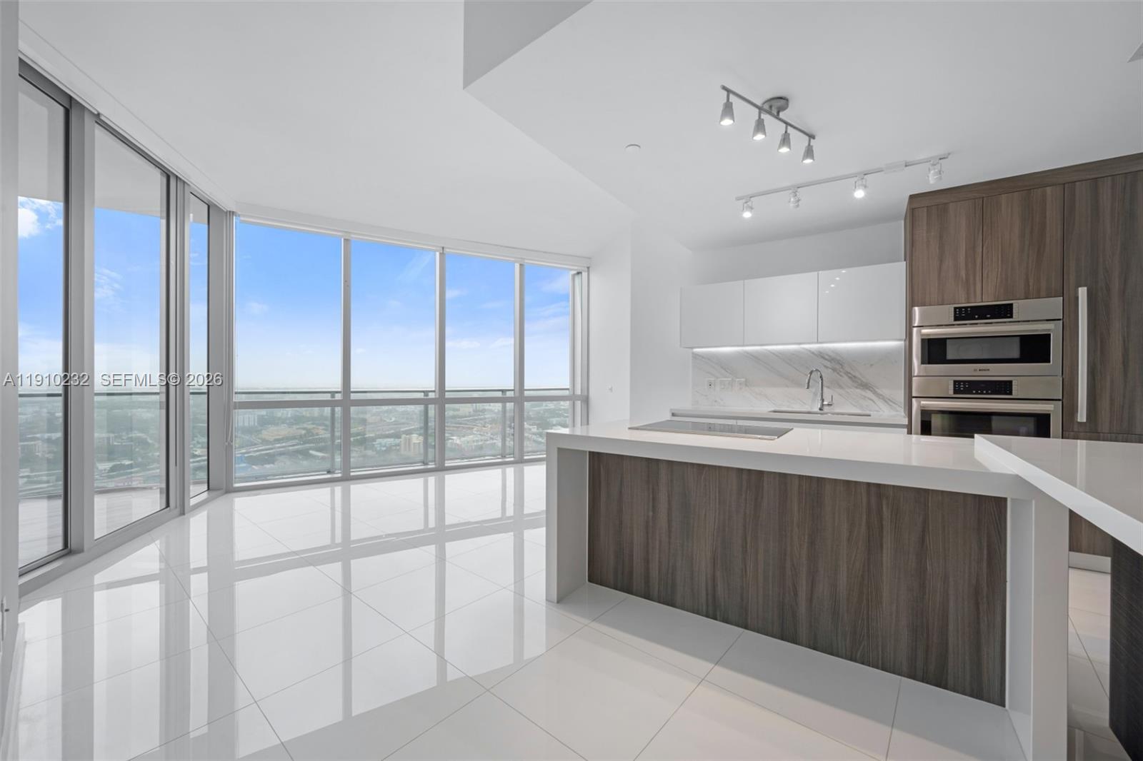 A modern kitchen features a waterfall island, wood-toned cabinetry, and floor-to-ceiling windows with city views — 851 NE 1st Ave # 4204, Miami FL 33132, MIAMI, FL