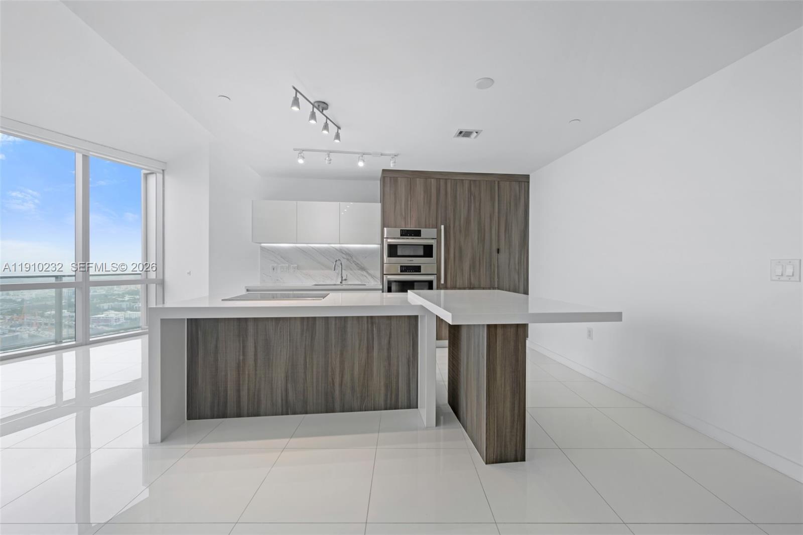 A modern kitchen features white cabinets, wood-grain paneling, a waterfall island, and floor-to-ceiling windows — 851 NE 1st Ave # 4204, Miami FL 33132, MIAMI, FL