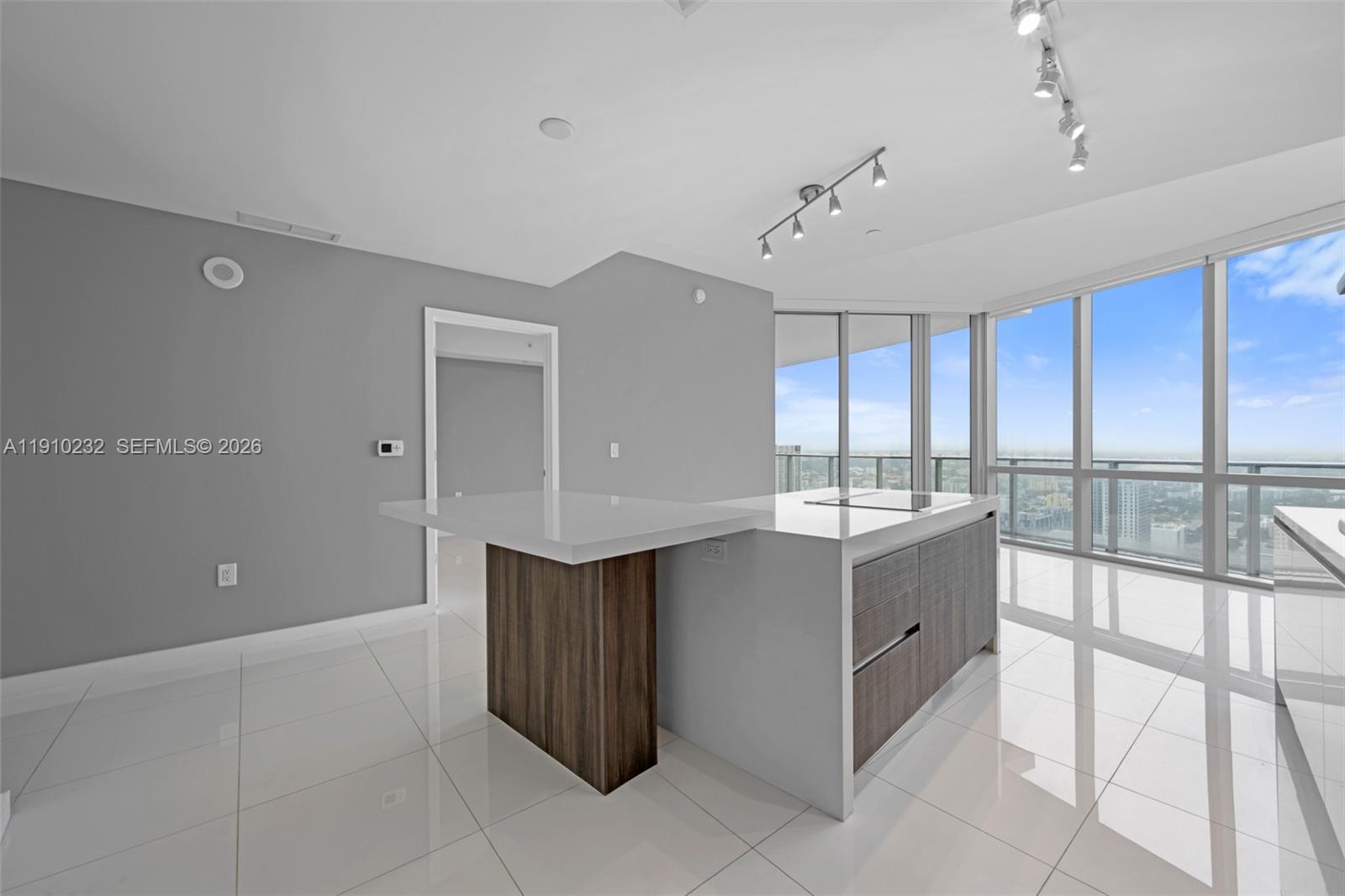 A modern kitchen features a white waterfall island with wood accents and floor-to-ceiling windows — 851 NE 1st Ave # 4204, Miami FL 33132, MIAMI, FL