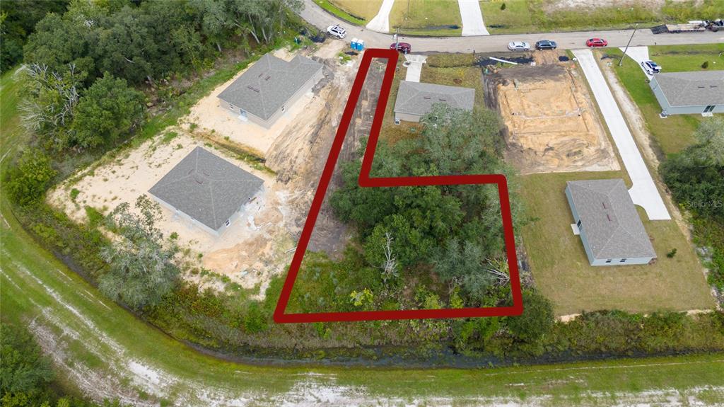 An aerial view shows a vacant, wooded residential lot outlined in red within a neighborhood — 133 SPARROW COURT, KISSIMMEE, FL