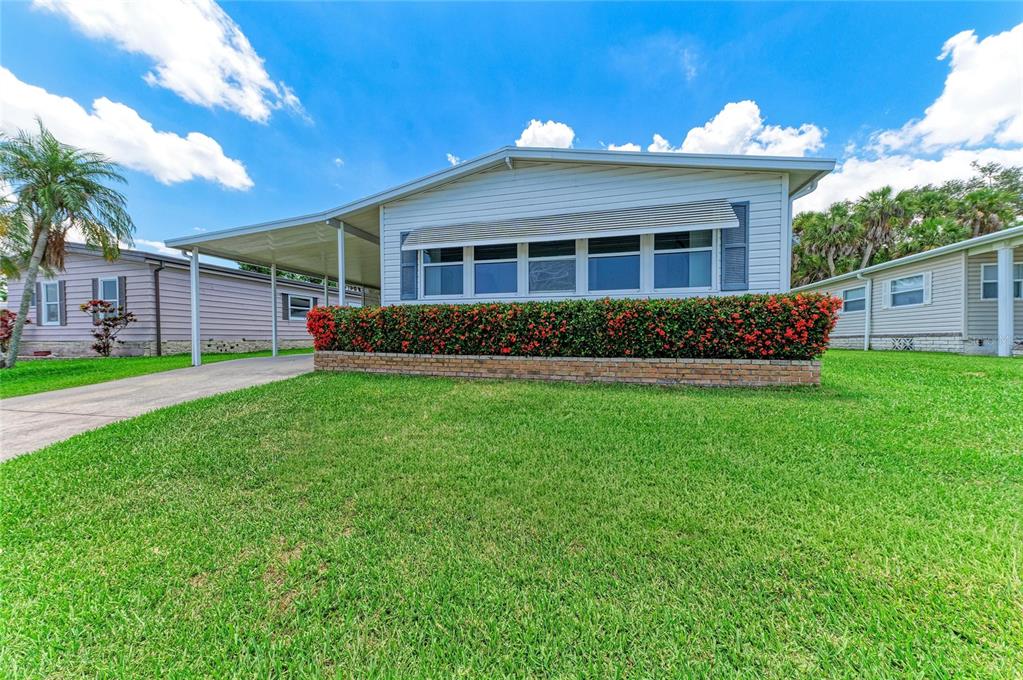 A single-story manufactured home with a carport, a brick planter, and a red-flowered hedge — 4543 12TH STREET COURT E, ELLENTON, FL