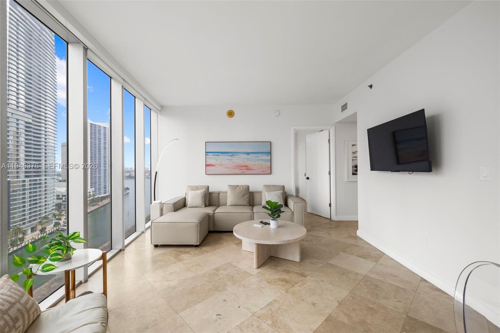 A modern living room features a sectional sofa, a round coffee table, and floor-to-ceiling windows — 485 Brickell Ave # 1804, Miami FL 33131, MIAMI, FL