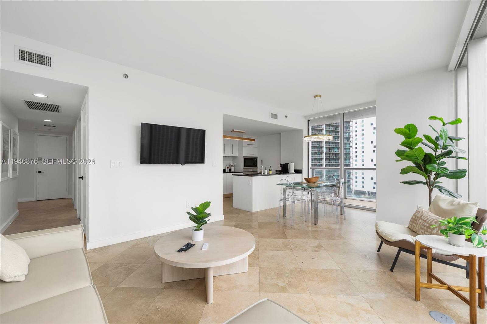 A bright living room features tile floors, a wall-mounted television, and an open-concept kitchen — 485 Brickell Ave # 1804, Miami FL 33131, MIAMI, FL