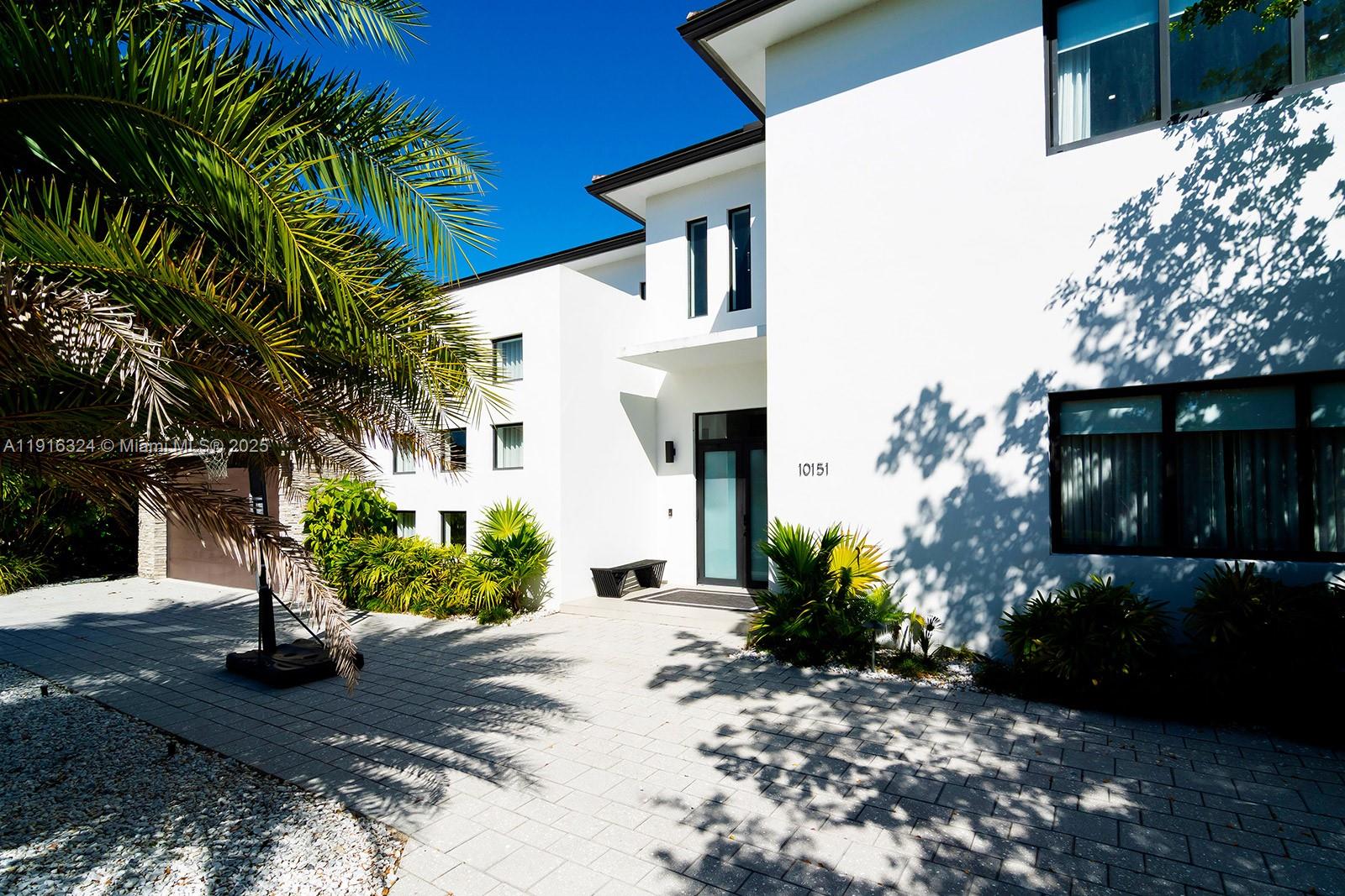 A modern white two-story house features a paved driveway, palm tree, and front entrance — 10151 SW 3rd St, Plantation FL 33324, PLANTATION, FL