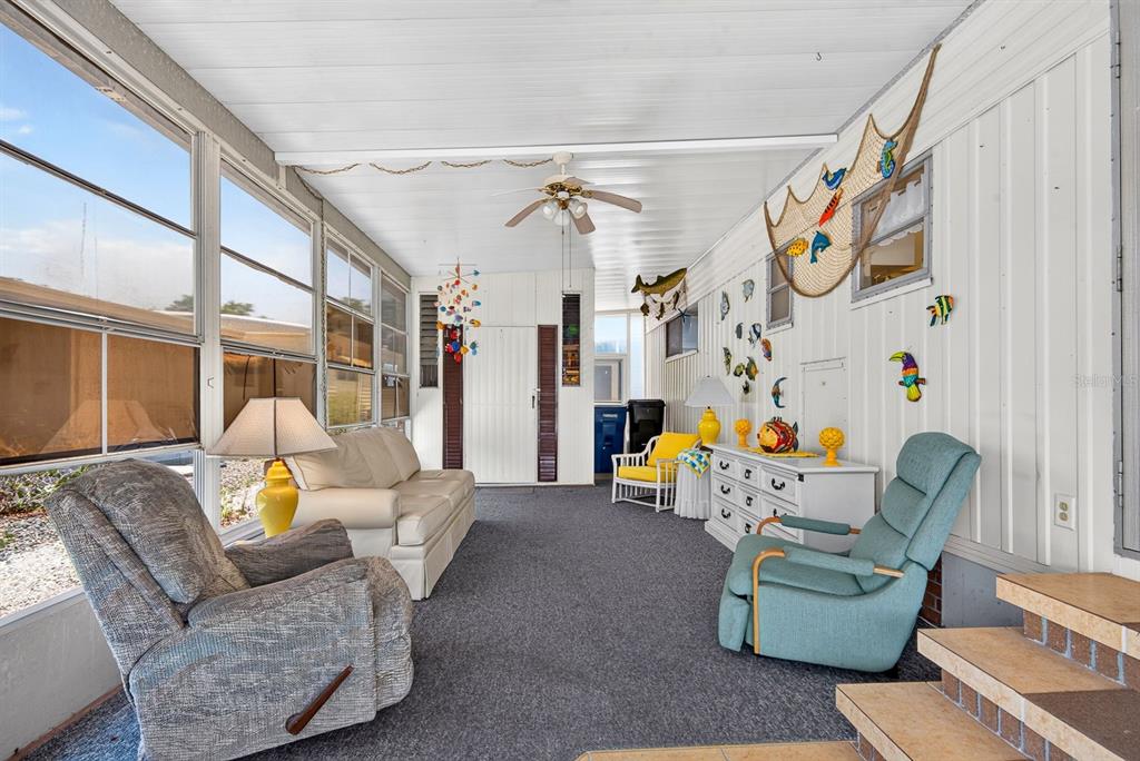 A sunroom features gray carpeting, white paneled walls, a ceiling fan, and nautical-themed wall decor — 37 CABALLO WAY, BRADENTON, FL