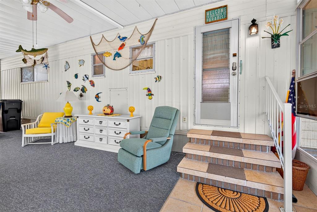 A covered porch features gray carpeting, a white dresser, a recliner, and nautical wall decor — 37 CABALLO WAY, BRADENTON, FL