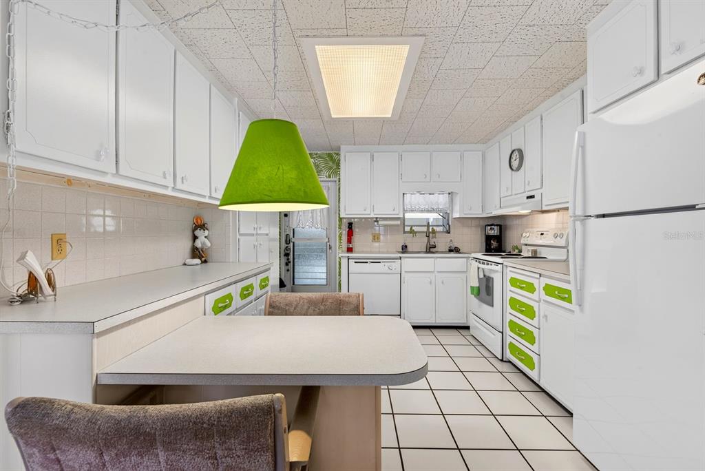 A kitchen features white cabinetry with green accents, a breakfast bar, and white tile flooring — 37 CABALLO WAY, BRADENTON, FL